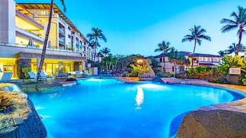 A hotel with a large swimming pool, palm trees, and multiple balconies.