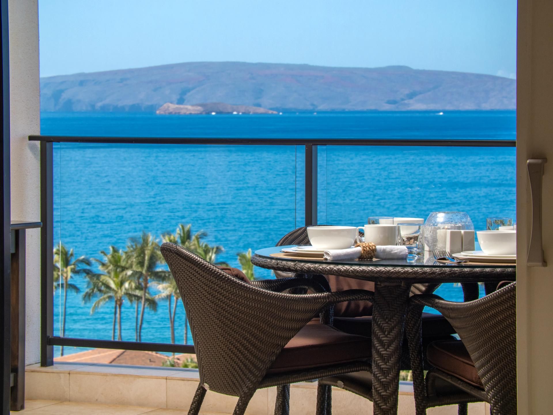 Un comedor con una mesa lista para cuatro personas, con vistas a un cuerpo de agua y un telón de fondo montañoso.