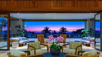 Ein moderner Außenbereich zum Sitzen mit Blick auf einen Sonnenuntergang über dem Meer, ausgestattet mit Korbstühlen und einem zentralen Tisch mit Blumenvase.