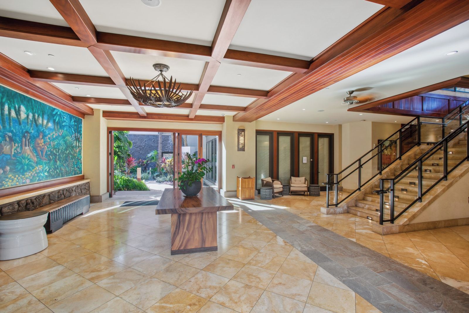 A spacious lobby with a large wooden reception desk, a staircase, and a mural on the wall.