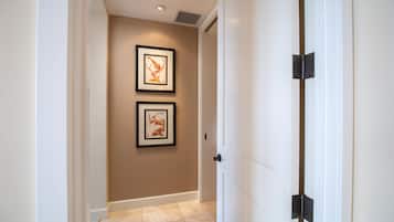 A hallway with two framed artworks on the wall, a white door with a black handle, and beige tiled flooring.