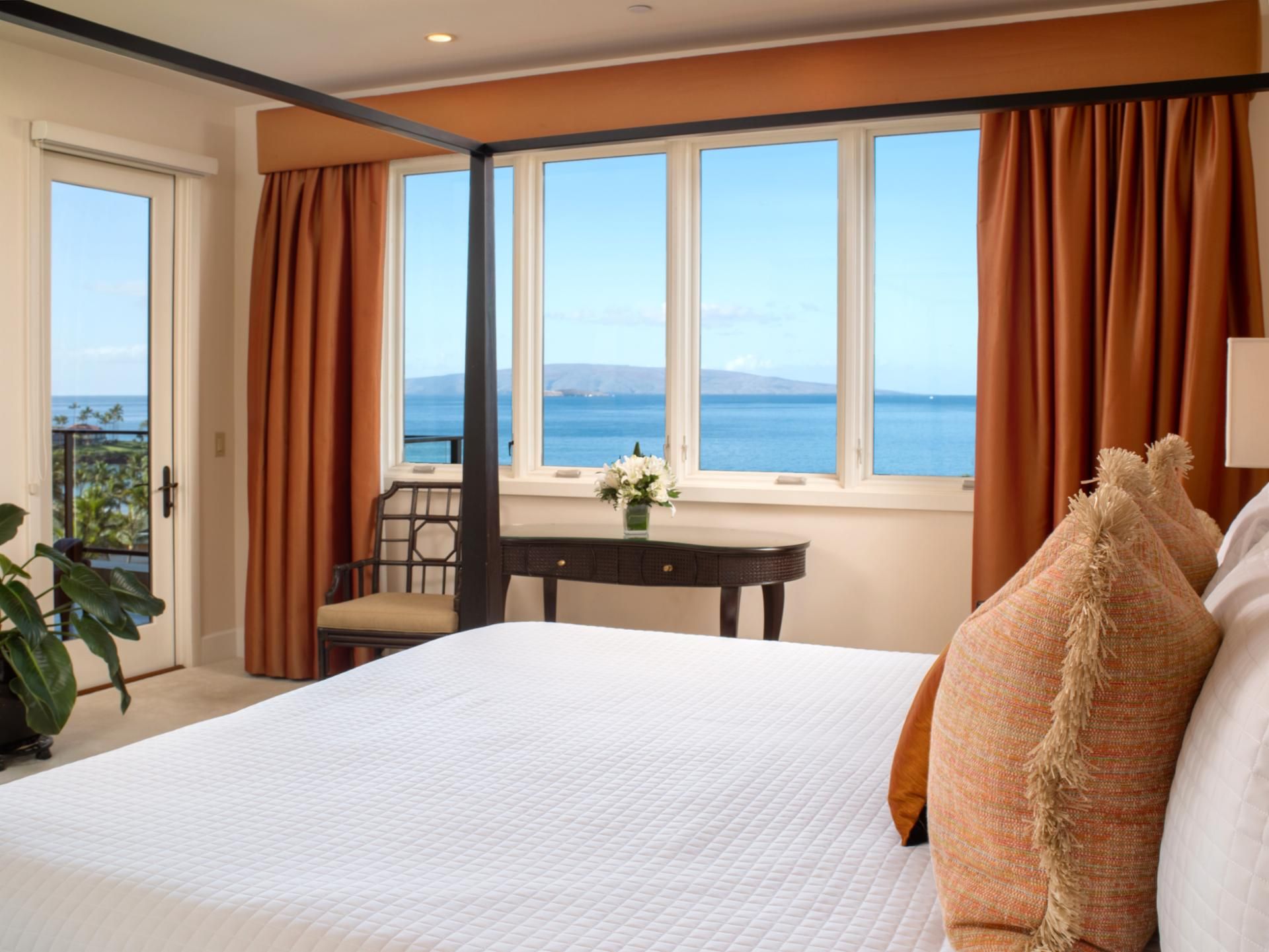 A hotel room with a large bed, a desk, and a view of the sea.