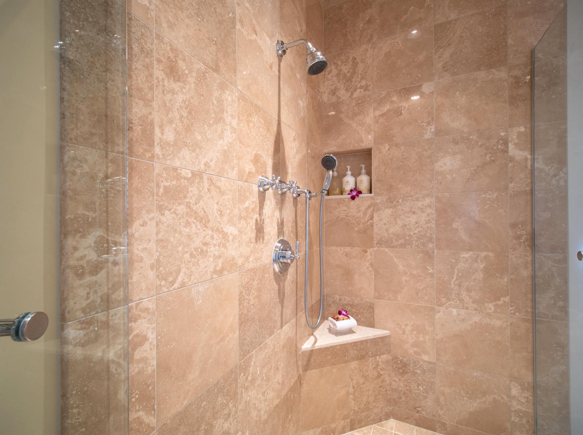 A shower with a handheld showerhead, a wall-mounted showerhead, and a glass-enclosed shower stall.