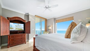 Een slaapkamer met een groot bed, een houten dressoir, een plafondventilator en uitzicht op de oceaan.