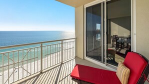Een balkon met uitzicht op de oceaan, een rode stoel en een schuifdeur naar een binnenruimte met een tafel en stoelen.