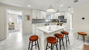 Een moderne keuken met witte kasten, een centraal eiland met krukken en hanglampen.