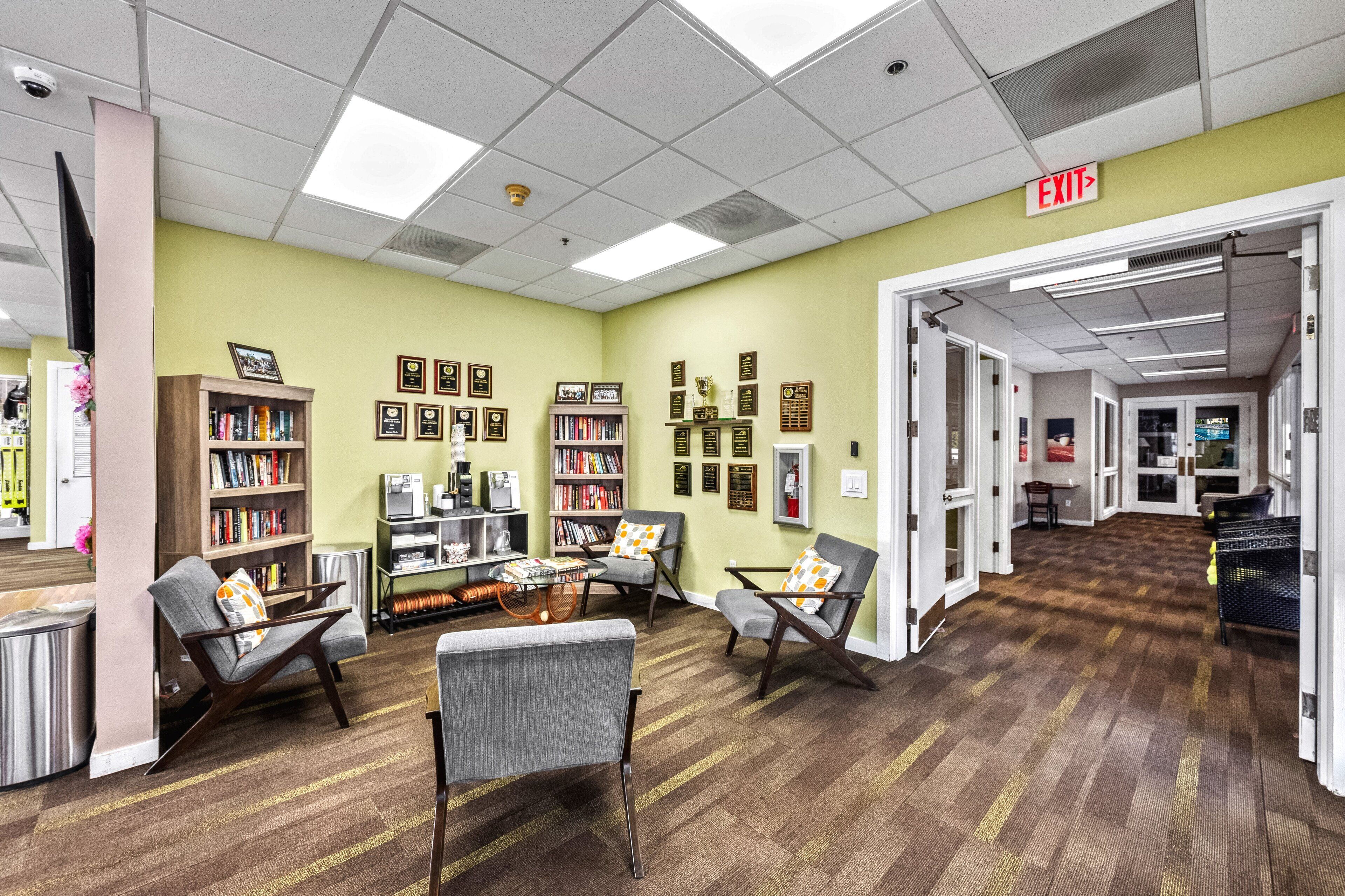 A library with bookshelves, reading chairs, and an exit sign.