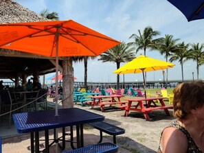 A beachside dining area with colorful tables and umbrellas, overlooking the ocean. - Ideal location - 2bed/1bath near the beach & shops (Port Charlotte)