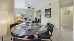 A spacious living room with a glass-top dining table, comfortable seating, a ceiling fan, and artwork on the walls. - Ideal location - 2bed/1bath near the beach & shops (Port Charlotte)