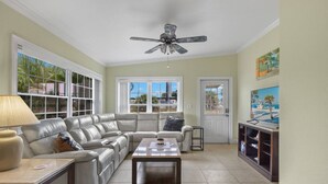 A spacious living room with a sectional sofa, a coffee table, a TV, and a ceiling fan. - Ideal location - 2bed/1bath near the beach & shops (Port Charlotte)