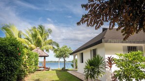 A white building with a thatched-roof structure in a lush garden by a lake. - Paradise (Bora Bora)