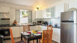A modern kitchen with white cabinets, a stainless steel refrigerator, and a dining area with wooden chairs and a table set for two. - Paradise (Bora Bora)