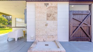 Une cabine de douche en pierre avec une porte en bois, une chaise en plastique blanche et une petite table sur une terrasse en béton.