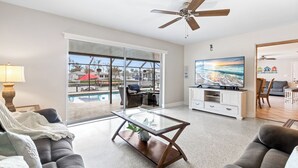 Ein geräumiges Wohnzimmer mit Glastür zum Poolbereich, Deckenventilator und Fernseher.