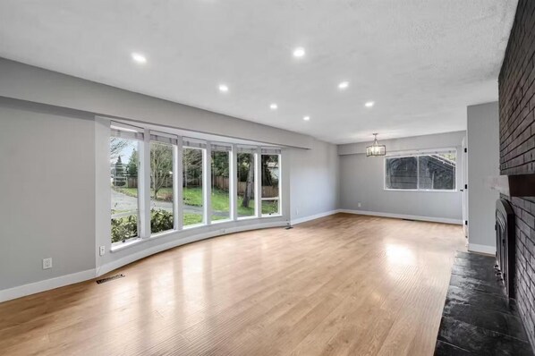 A spacious room with large windows, a wooden floor, and a fireplace.