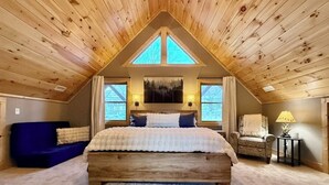 Une chambre avec un plafond en bois, un grand lit, un canapé bleu et un fauteuil.