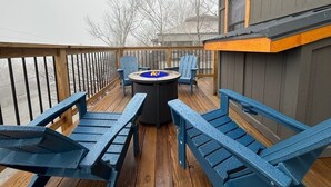 Une terrasse avec un foyer, des fauteuils Adirondack bleus et une vue sur l’eau.