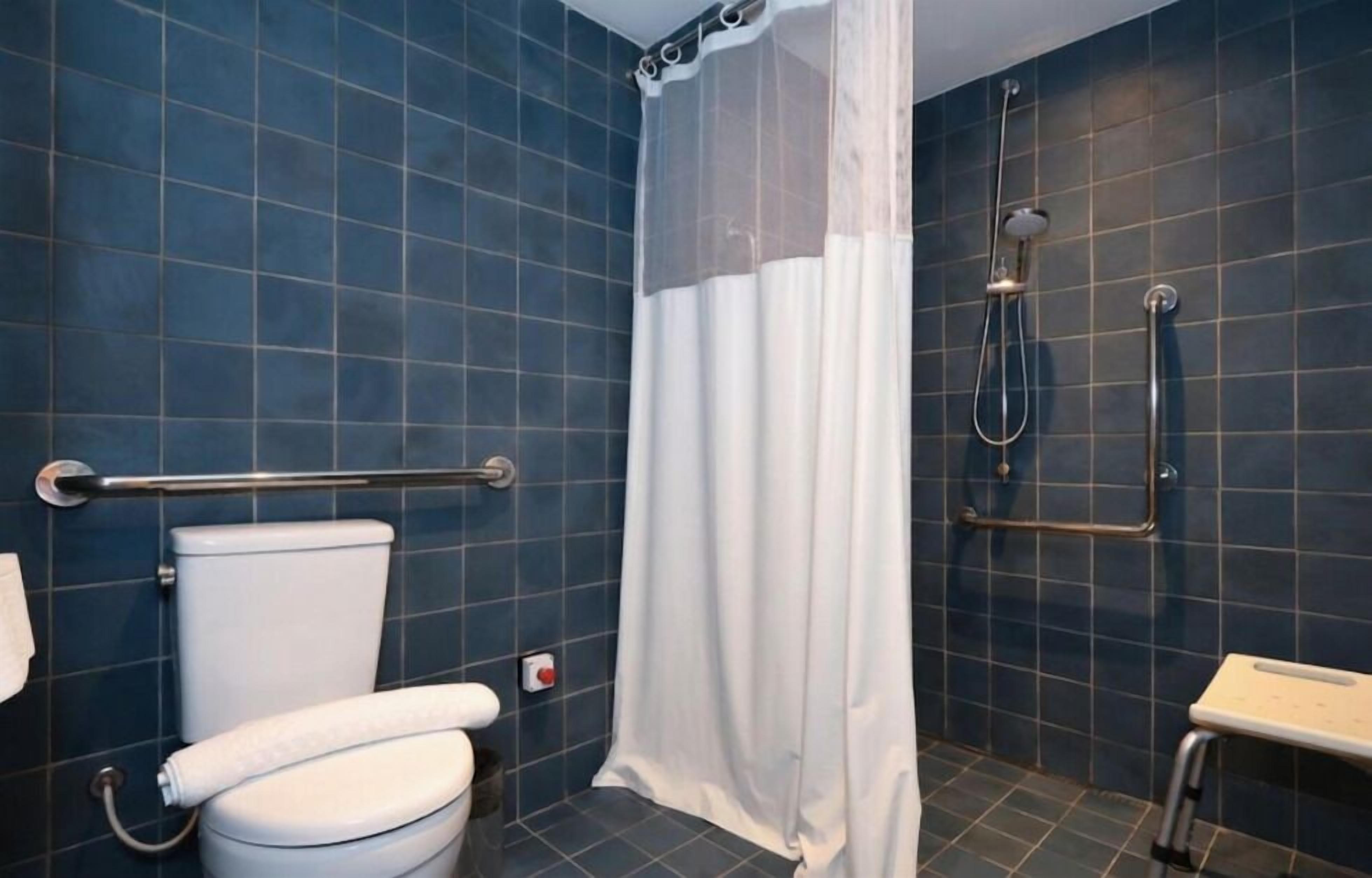 Un baño con inodoro, ducha y barras de apoyo.