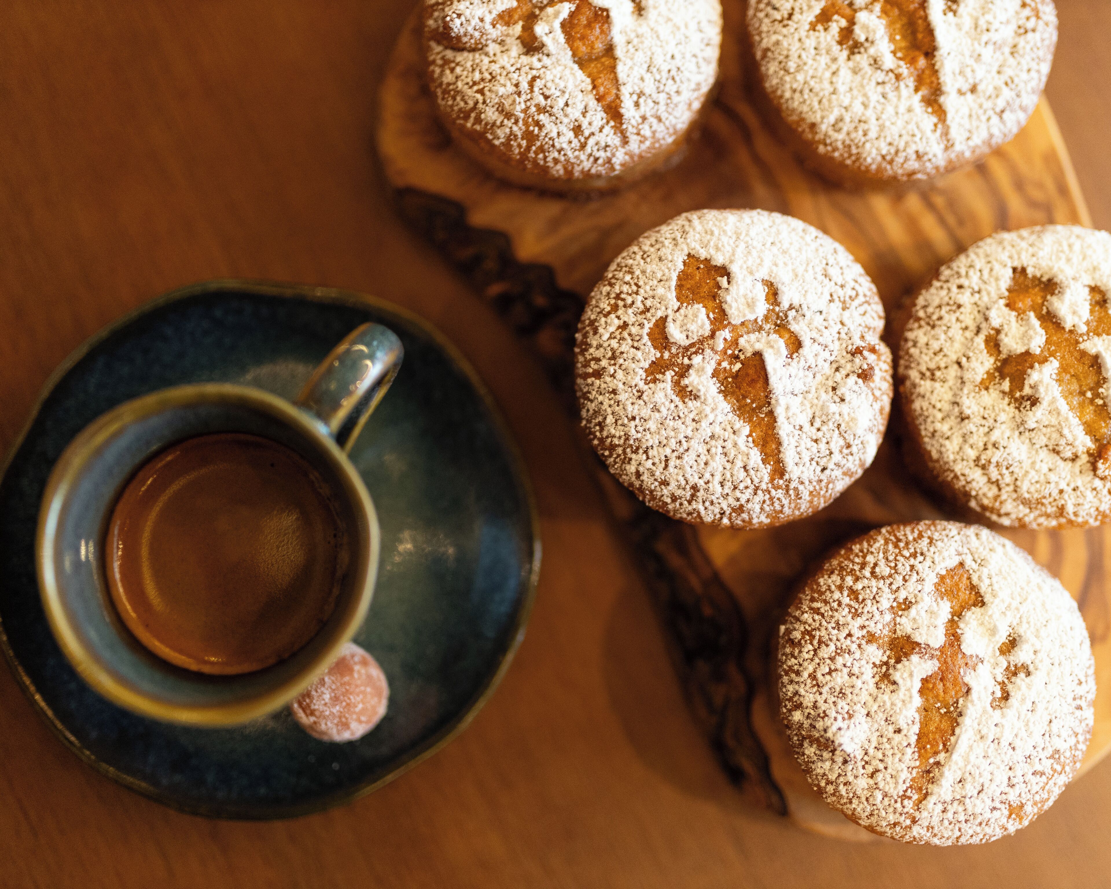 Una taza de café sobre un plato con una bandeja de pasteles redondos espolvoreados con azúcar glas.
