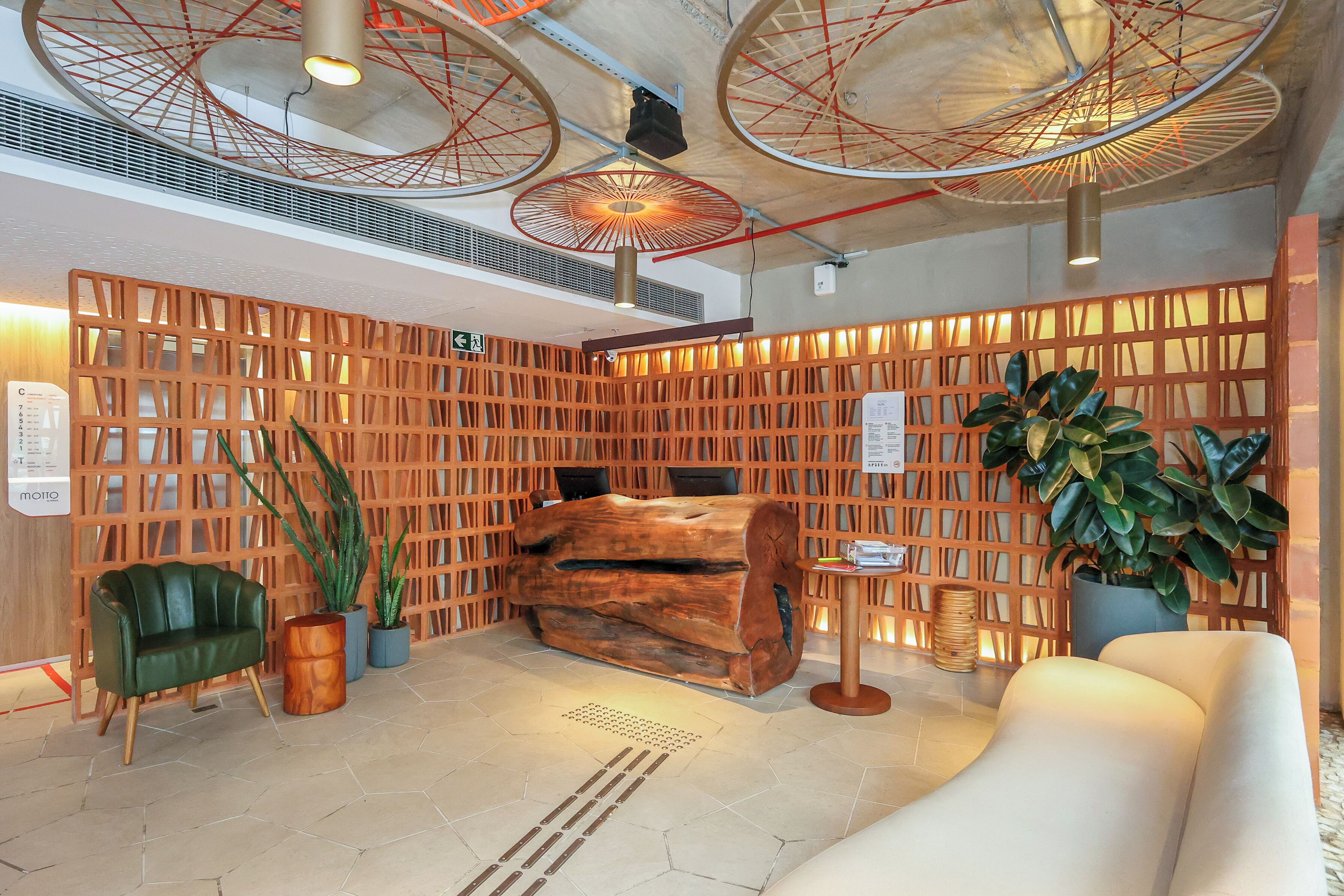 Um lobby moderno com uma mesa de recepção de madeira, uma cadeira verde, um sofá e uma grande planta em vaso.