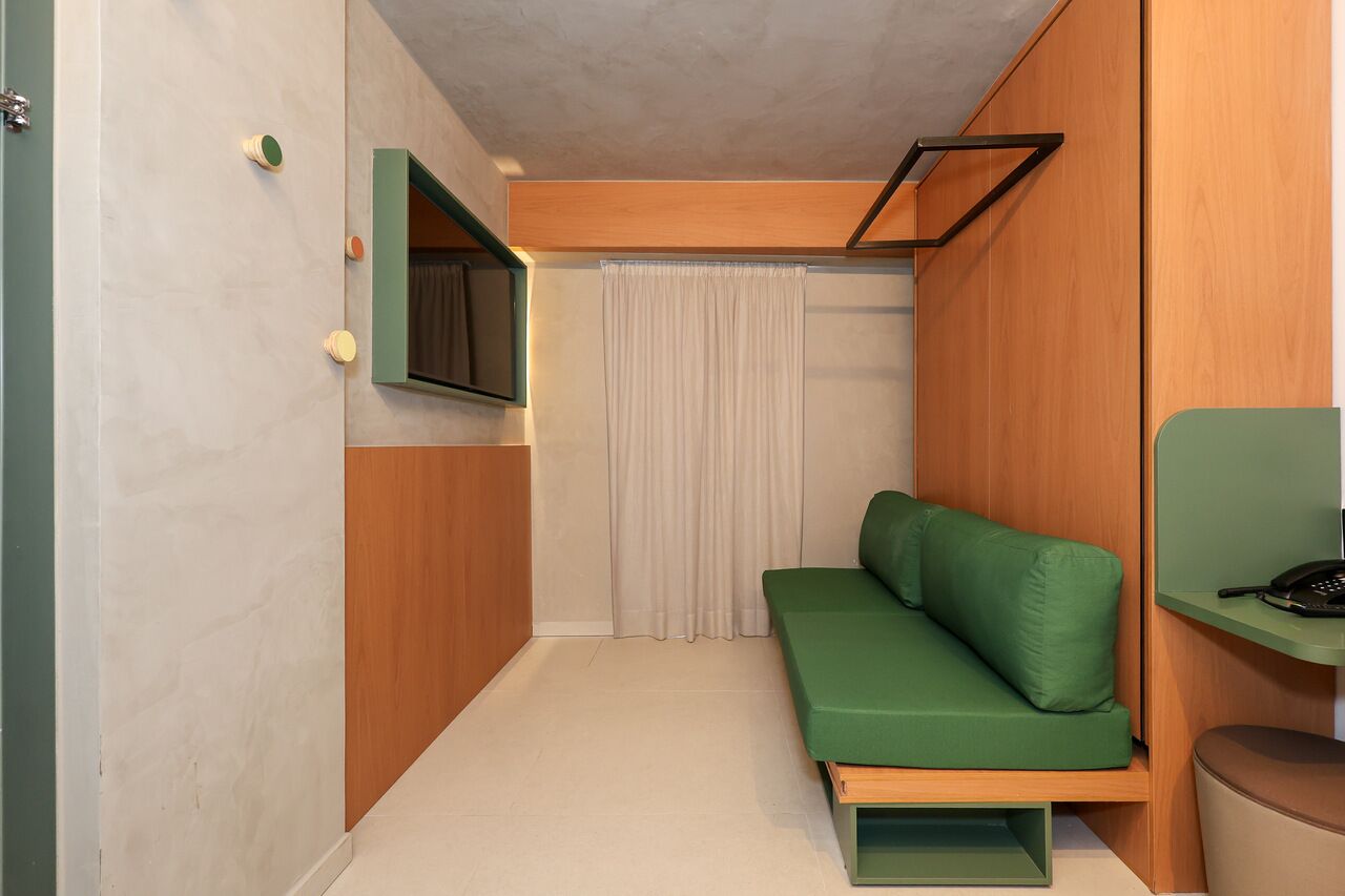 A compact room with a green sofa, a small table with a phone, a TV mounted on the wall, and a curtain.