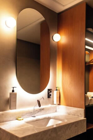 A modern bathroom with a large oval mirror, a marble sink, and wooden paneling. - Motto By Hilton Recife (Recife)