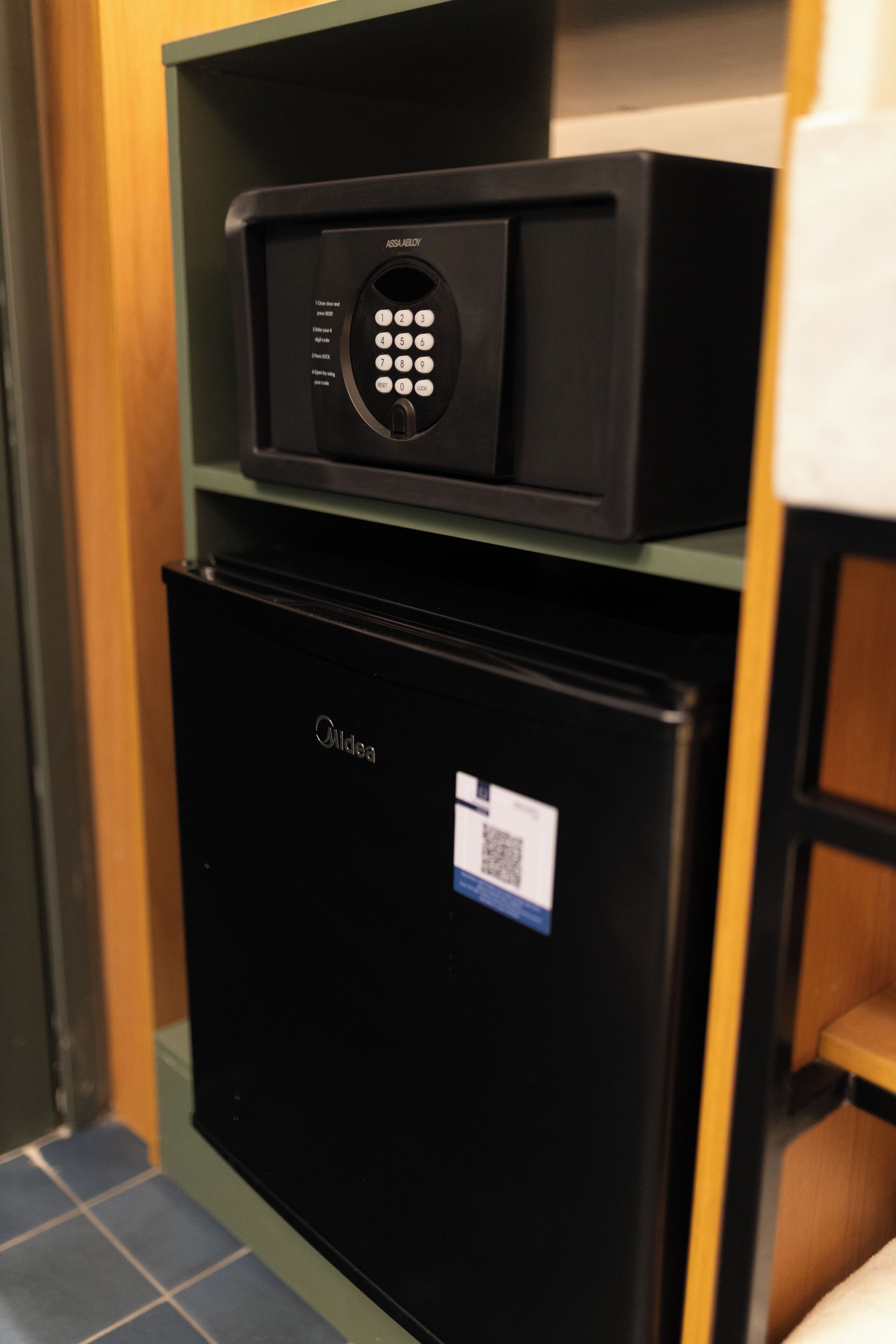 Ein schwarzer Kühlschrank mit einem darunterliegenden Gefrierfach, eine schwarze Mikrowelle darüber und ein QR-Code-Aufkleber am Kühlschrank.