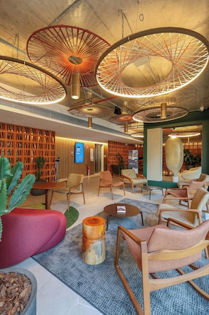 A modern lobby with circular ceiling lights, seating areas, and a digital information kiosk.