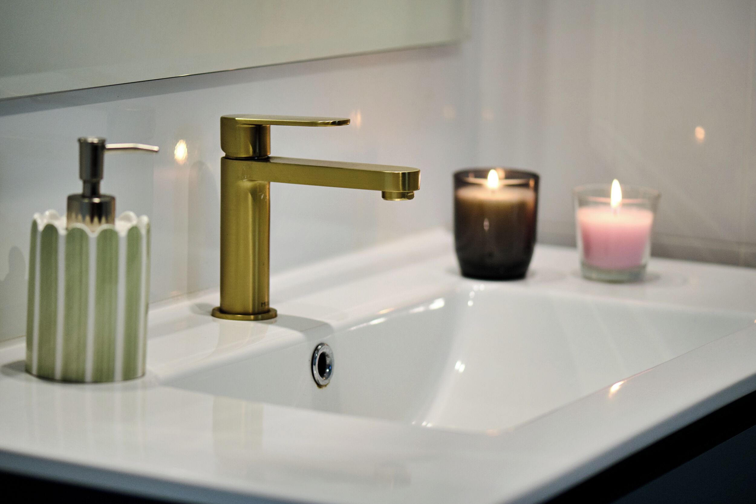 A bathroom sink with a gold faucet, a green striped soap dispenser, and two lit candles.
