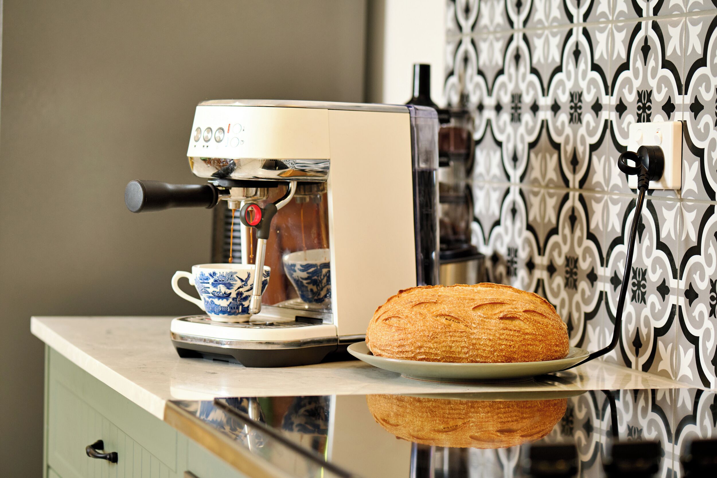 Una cocina con cafetera, un plato con hogaza de pan y un salpicadero decorado.