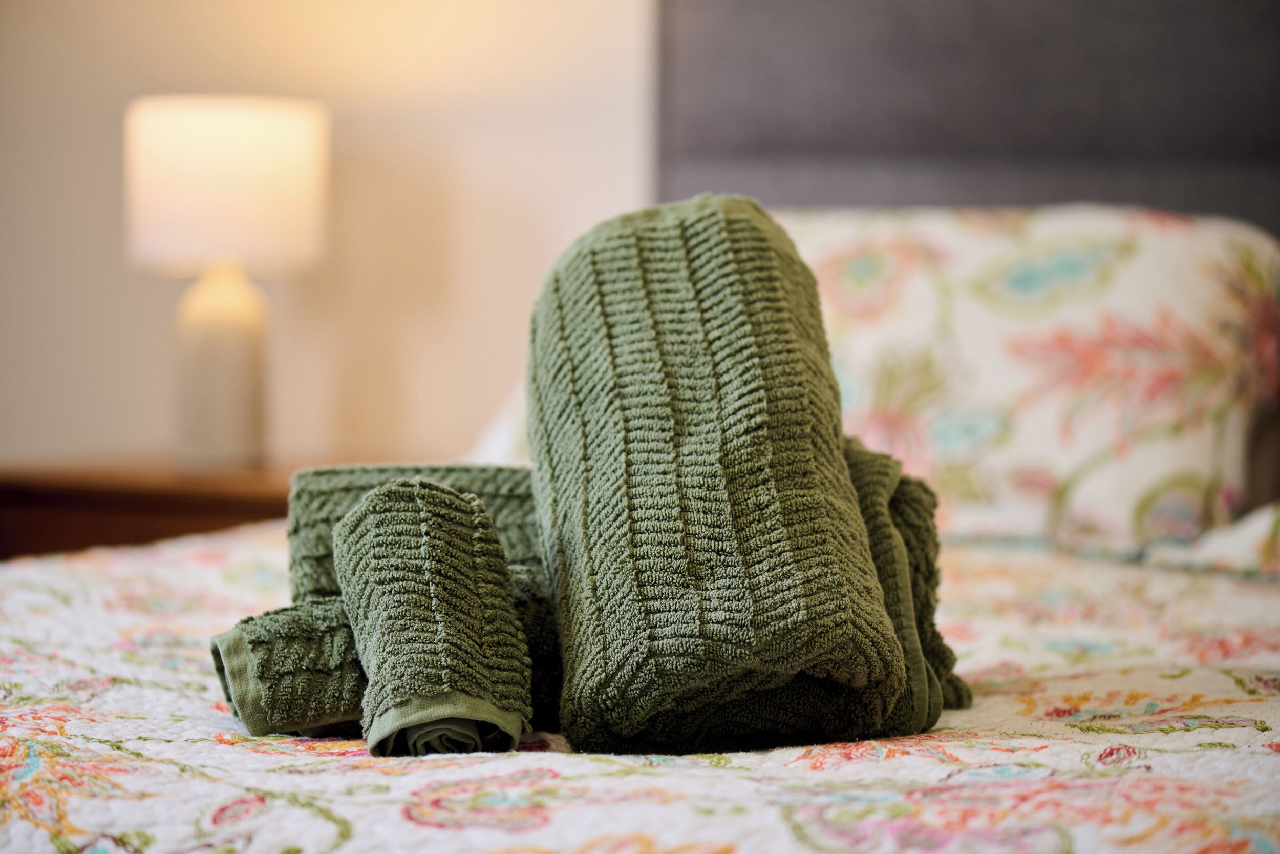 Una cama con una colcha estampada de flores y una manta verde de punto.