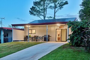 Una casa moderna con patio coperto, zona barbecue e prato curato.