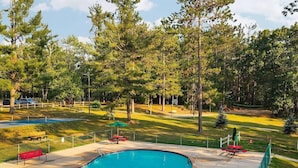 A swimming pool with a wooden deck, surrounded by grass and trees. - Delightful 4-bedroom house in Gaylord Michigan perfect for large families (Gaylord)