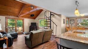 A spacious living room with a fireplace, a sofa, a dining area with a kitchen island, and a staircase leading to an upper level. - Delightful 4-bedroom house in Gaylord Michigan perfect for large families (Gaylord)