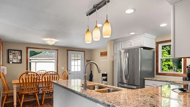 A kitchen with a granite countertop, stainless steel appliances, wooden chairs, and pendant lighting. - Delightful 4-bedroom house in Gaylord Michigan perfect for large families (Gaylord)