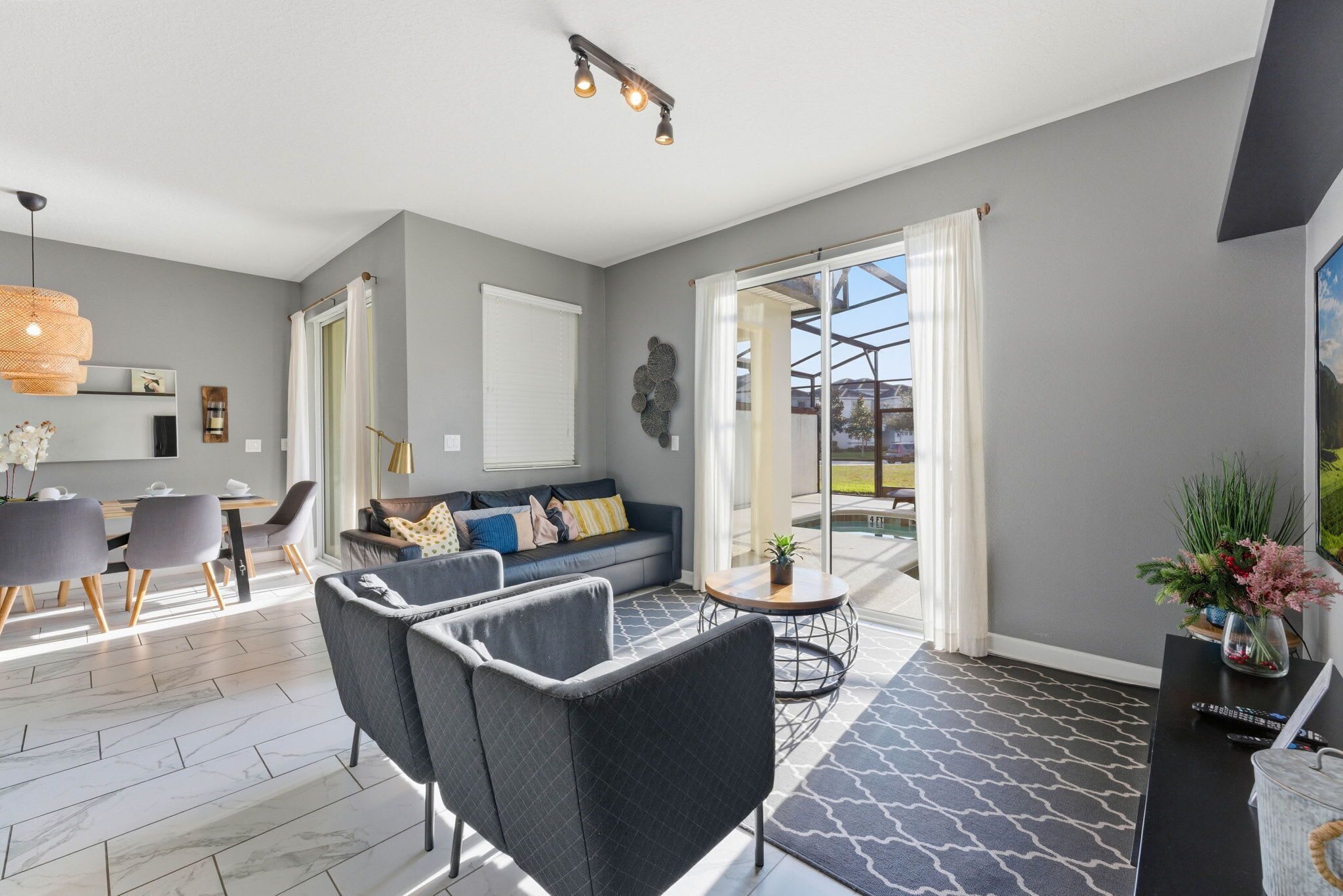 A modern living room with a sofa, a dining area with chairs, a coffee table, and a large window with curtains.