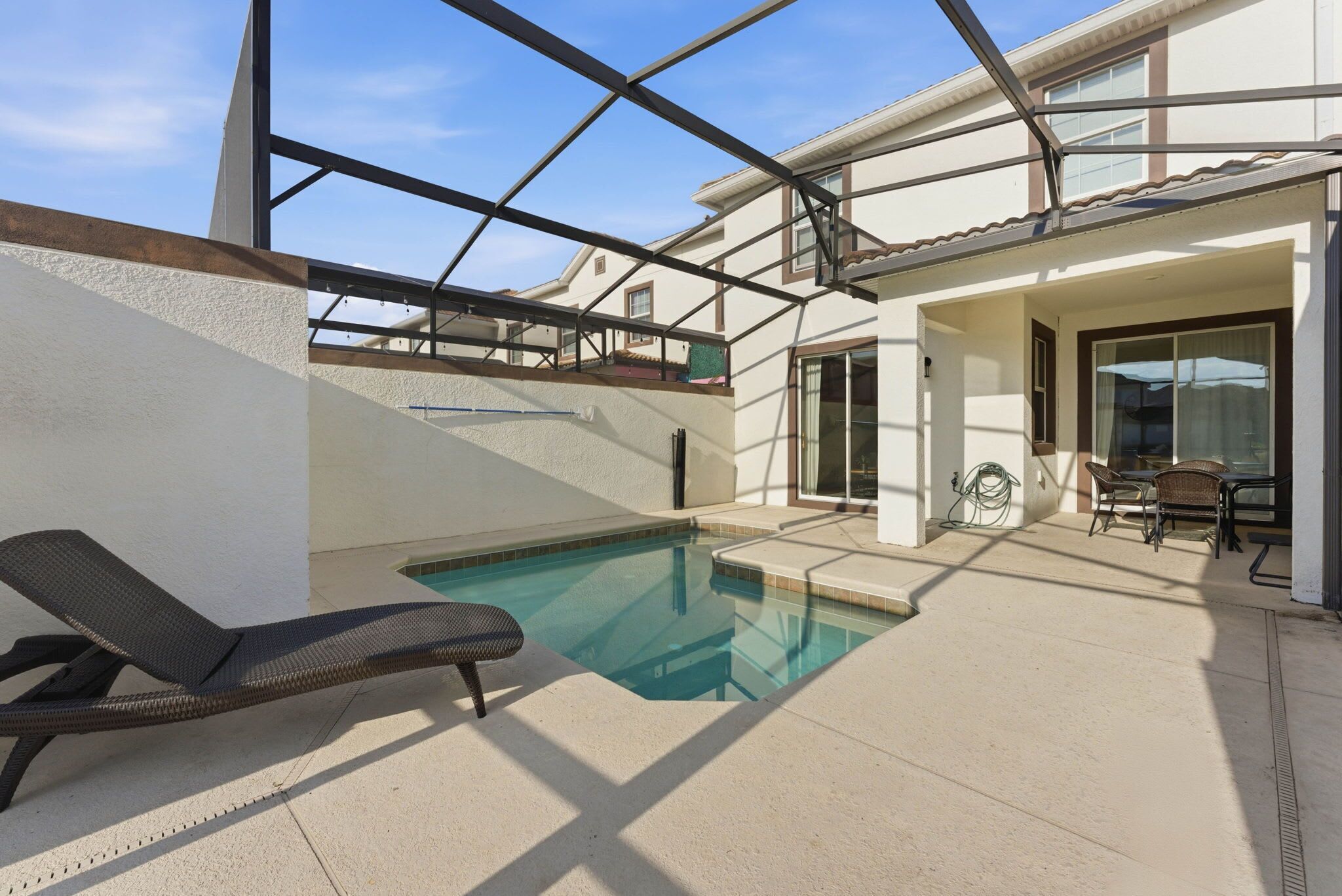 An outdoor swimming pool area with a lounge chair, a covered patio, and a view of the building's exterior.