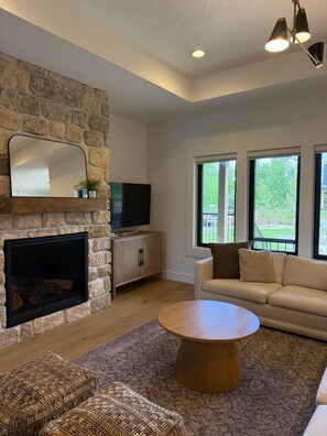 A living room with a stone fireplace, a television, a sofa, and a coffee table. - Cabin w/Hot Tub & Bunk Room - Steps to the lake! (Valley County)
