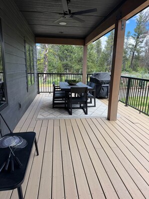 A covered outdoor deck with a table and chairs, a ceiling fan, and a grill. - Cabin w/Hot Tub & Bunk Room - Steps to the lake! (Valley County)