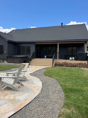 A modern house with a stone patio, outdoor seating, and a covered area. - Cabin w/Hot Tub & Bunk Room - Steps to the lake! (Valley County)