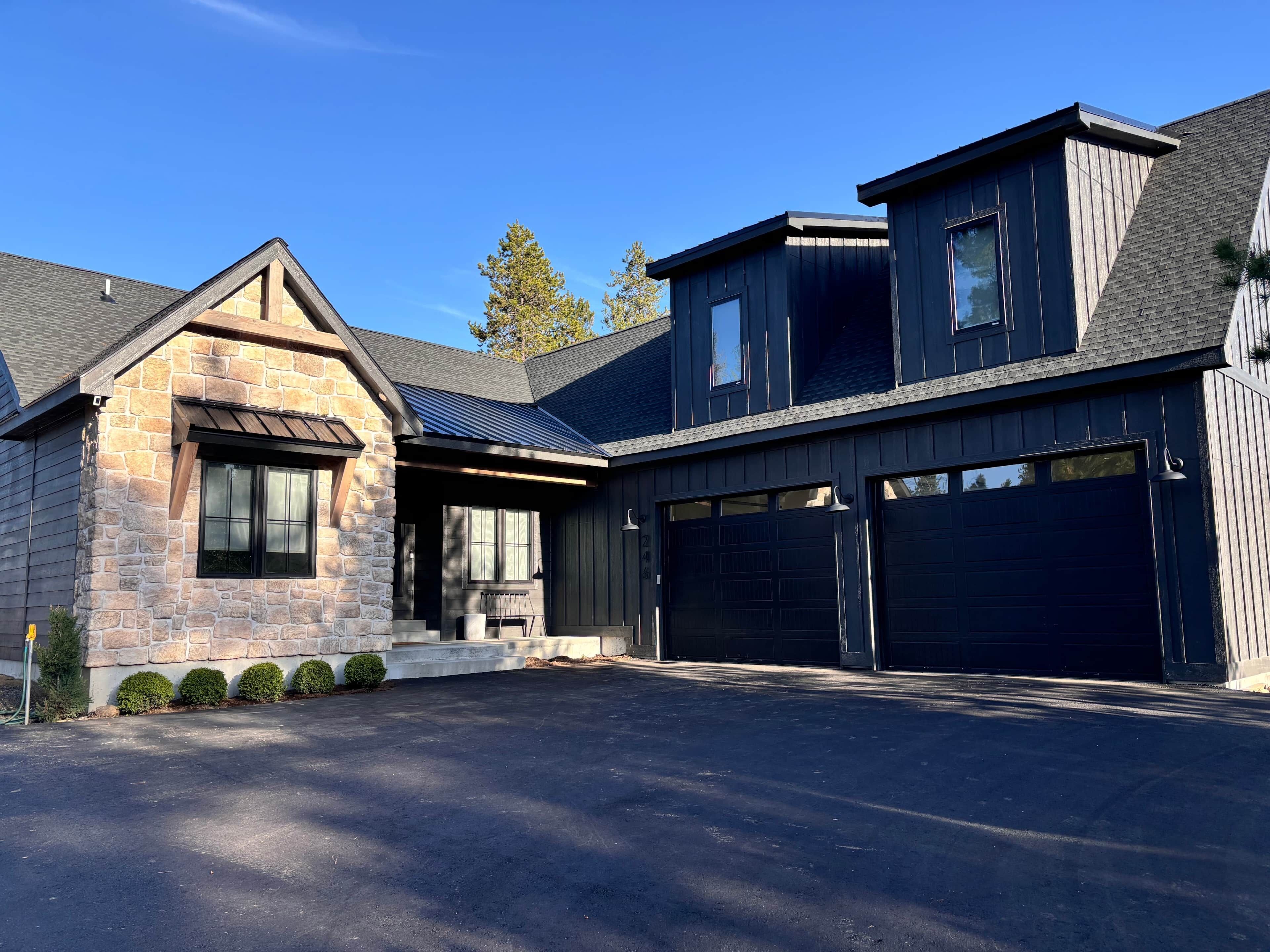 Une maison moderne à deux étages, dotée d’une façade en pierre, d’un garage à deux portes et d’un porche abrité.