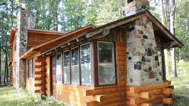 A rustic cabin with a stone chimney, wooden exterior, and large windows. - Delightful 3-bedroom cabin on Big Roche Cri Lake in charming Friendship, WI! (Friendship)