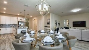 A modern dining area with a glass table, grey upholstered chairs, and a contemporary chandelier. - Storey Lake 6 Bedroom Vacation Home 4712 (Osceola County)