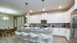 A modern kitchen with white cabinets, stainless steel appliances, and a marble countertop. - Storey Lake 6 Bedroom Vacation Home 4712 (Osceola County)