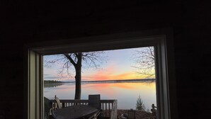 A window view of a lake with a dock and a tree, framed by a window with a white border.