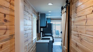 A narrow wooden hallway leading to a kitchen with a stove, cabinets, and a view of the outdoors.