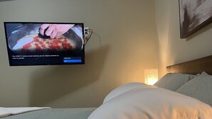Habitación de hotel con una cama, un televisor empotrado mostrando un video de cocina y una lámpara de noche.