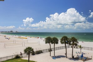 Ein Strand mit einer Umzäunung, Palmen und Sonnenschirmen.