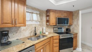 A kitchen with wooden cabinets, a stainless steel sink, a microwave, an oven, and a coffee maker. - 🌊 New Listing! Caprice Resort Unit #305 – Gulf Front Comfort with Private Balcony (Saint Pete Beach)