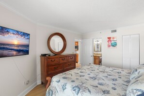 A bedroom with a bed, dresser, and a painting of a sunset over the ocean. - 🌊 New Listing! Caprice Resort Unit #305 – Gulf Front Comfort with Private Balcony (Saint Pete Beach)